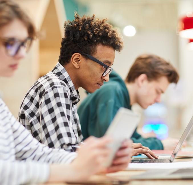 Trois étudiants travaillent sur des ordinateurs portables et tablettes